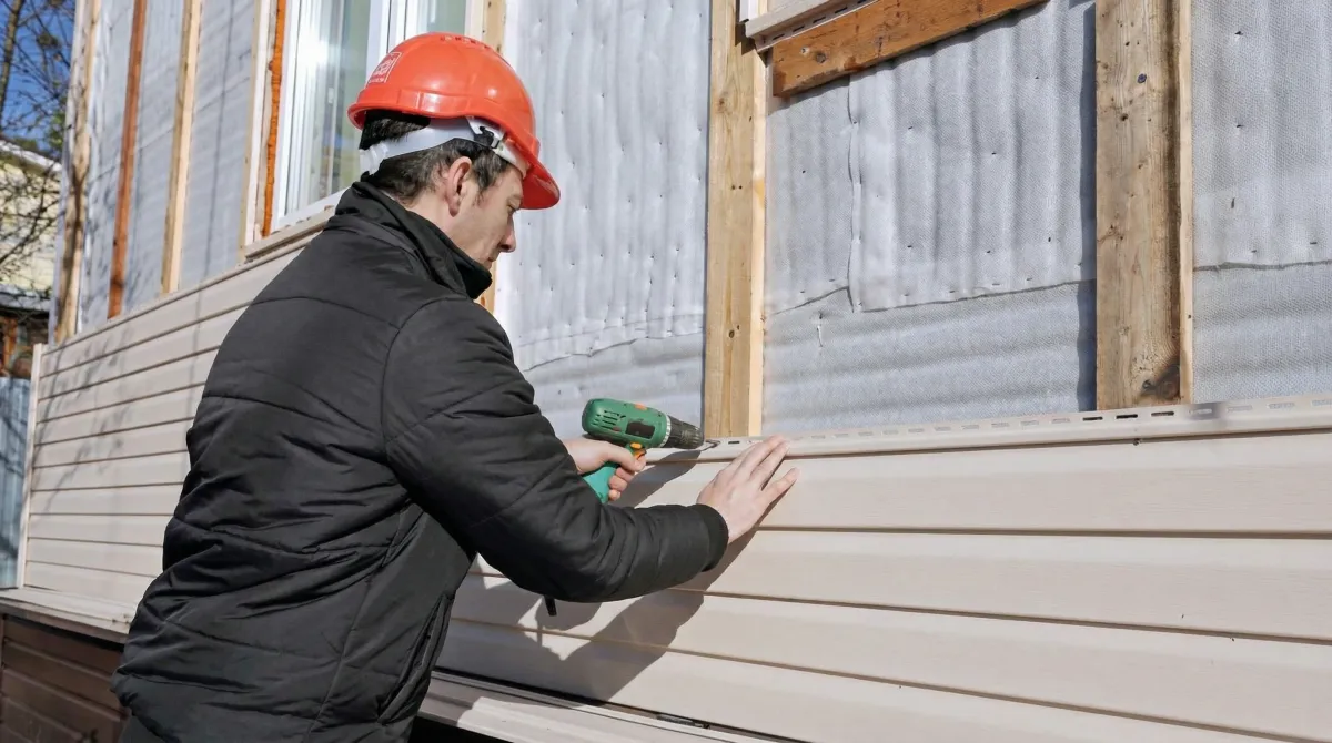 Siding replacement professional using a power drill to install new tan vinyl siding on a home exterior in Dallas, TX